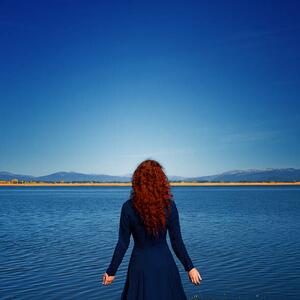 Fotográfia Redhead in blue dress faces rippled lake, Anna Gorin, (40 x 40 cm)