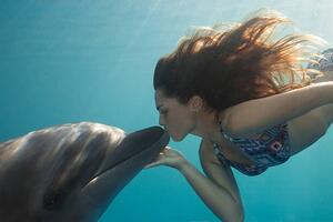 Fotográfia Young Woman Kisses Dolphin Underwater, Sunbeams, Justin Lewis, (40 x 26.7 cm)