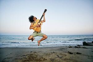 Művészeti fotózás Mixed Race man playing guitar and jumping at beach, Peathegee Inc, (40 x 26.7 cm)