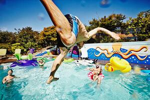 Fotográfia Man in mid air jumping into pool during party, Thomas Barwick, (40 x 26.7 cm)