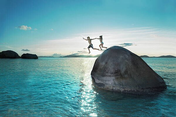Fotográfia Two kids holding hands jumping off rock into sea, Gary John Norman, (40 x 26.7 cm)